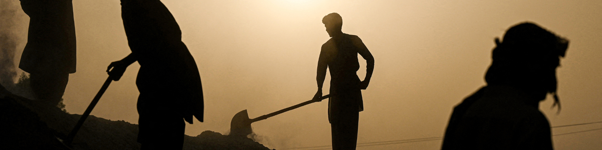 Silhouette of people with shovels working in the field, with the sun blazing in the background